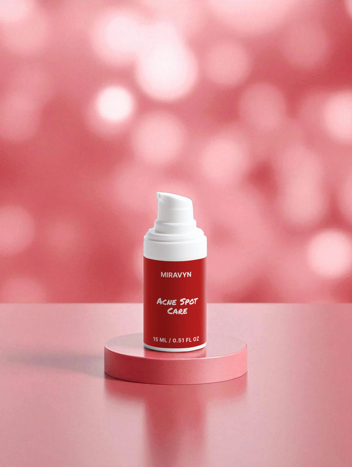 Red acne spot treatment cream bottle with white cap on a pink platform against a pink background.