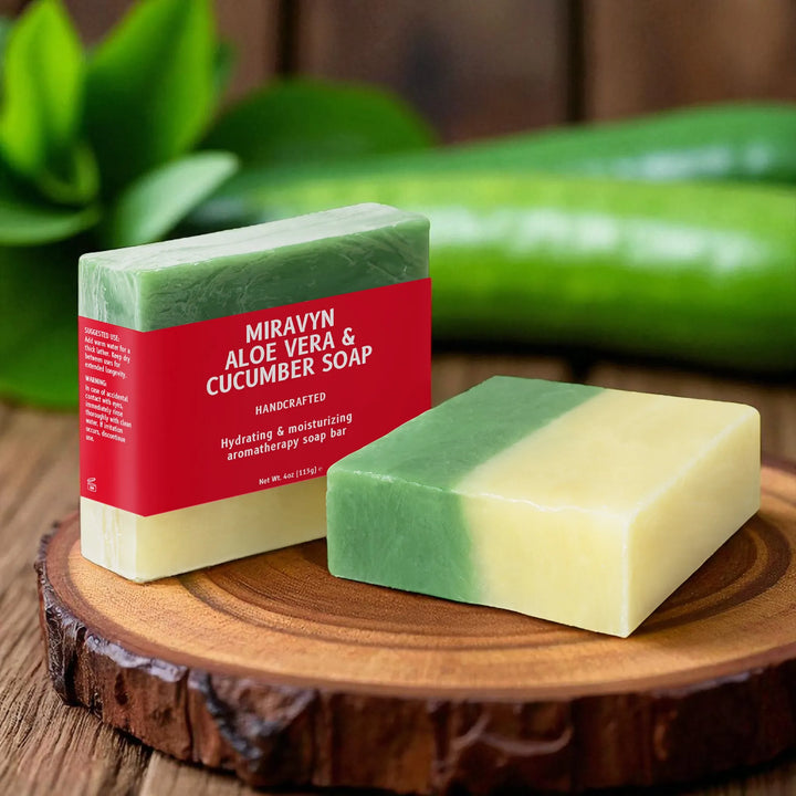 Two bars of Miravyn Aloe Vera & Cucumber Soap on a wooden surface with a blurred green background.