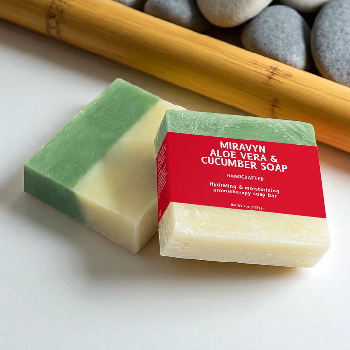Two soap bars with a red label on a light surface, with a bamboo stick and stones in the background.