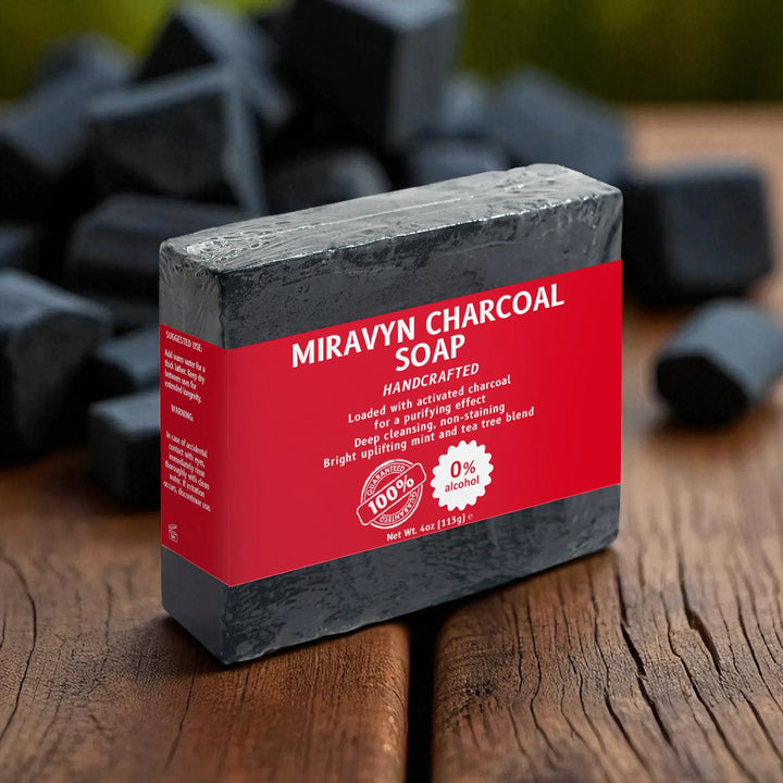Miravyn Charcoal Soap bar with red label on a wooden surface and charcoal behind it.