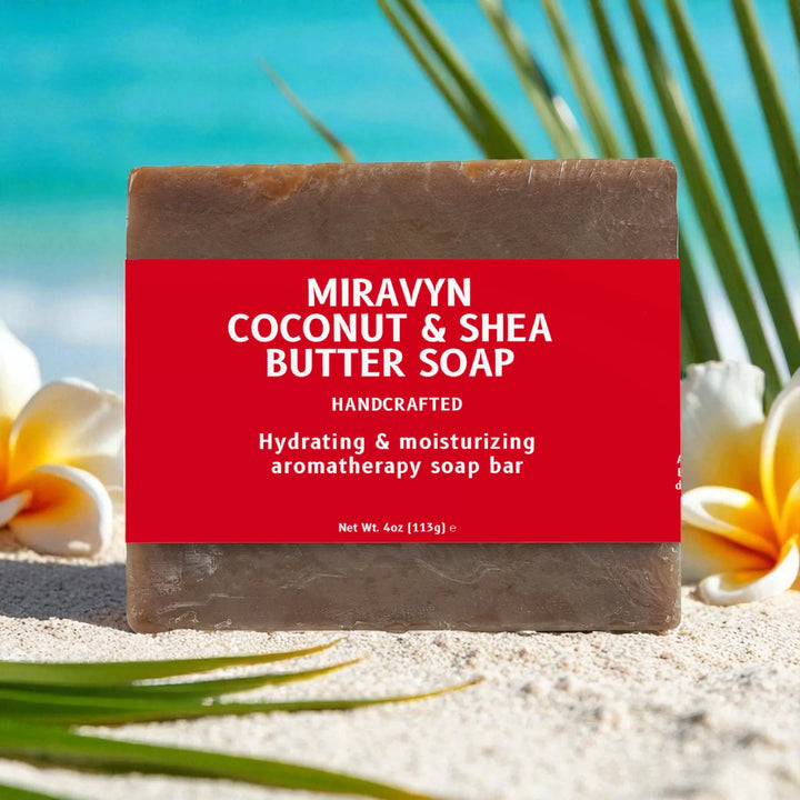 Miravyn coconut and shea butter soap bar with a red label on a sandy background with flowers and palm leaves.