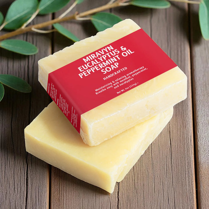Two bars of eucalyptus soap with a red label on a wooden surface with green leaves.