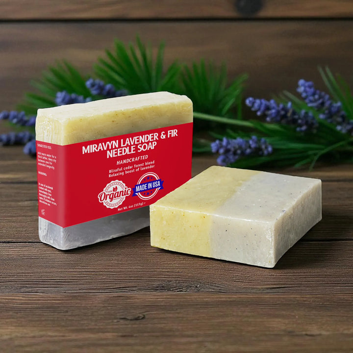 Two bars of lavender soap with a red label on a wooden surface with lavender flowers in the background.