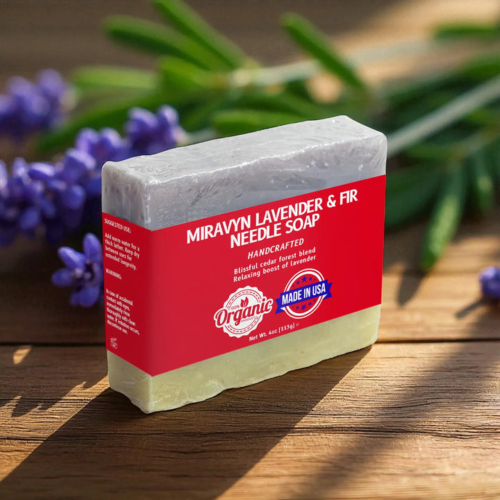Bar of Miravyn Lavender & Fir Needle Soap with red label on a wooden surface with lavender in the background.