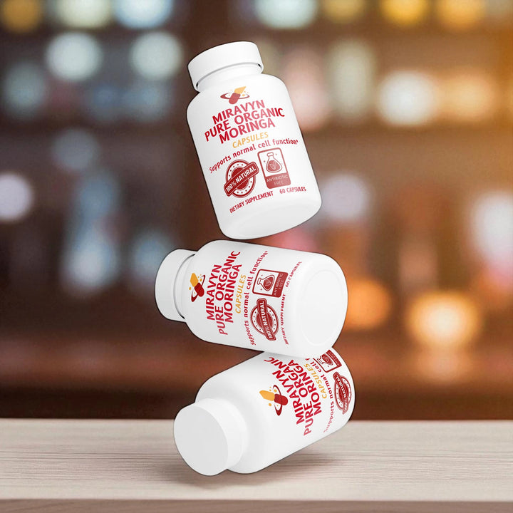 Three Miraval Pure Organic Moringa capsules with bottles stacked on a wooden surface under bokeh effect.