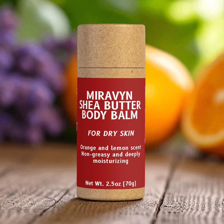 Miravyn Shea Butter Body Balm container on a wooden surface with fruits in the background.