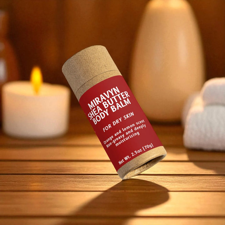 Miravyn Shea Butter Body Balm container on a wooden surface with a candle in the background.