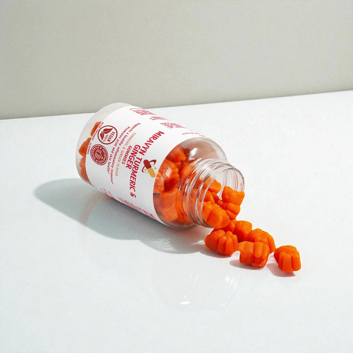 Orange turmeric and ginger gummies spilling out of a Miravyn jar on a white background.