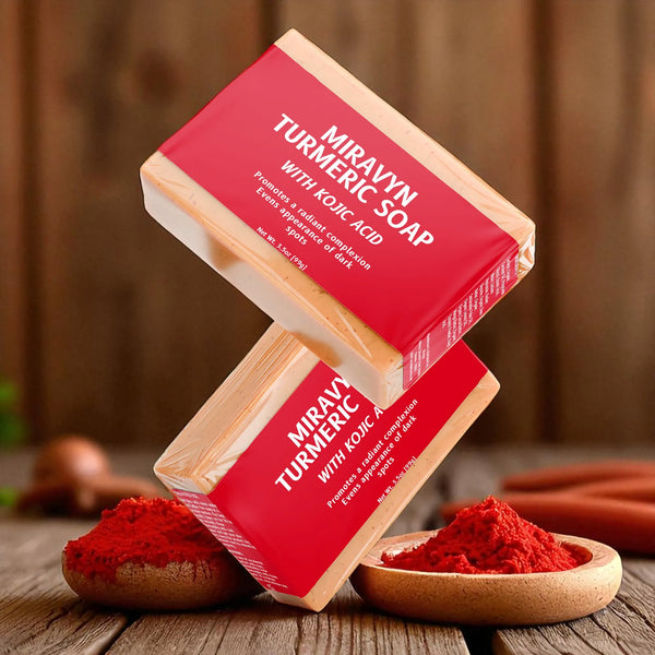 Two bars of Miravyn Turmeric Soap with Kojic Acid falling on a wooden surface with turmeric powder.