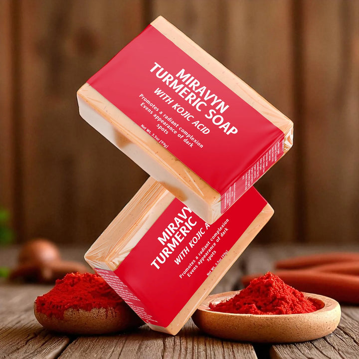 Two bars of Miravyn Turmeric Soap with Kojic Acid falling on a wooden surface with turmeric powder.